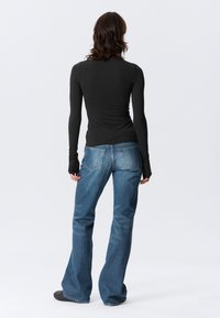 Haut rayé noir à manches longues associé à un jean bleu évasé. Le haut présente une coupe ajustée, et le jean possède des poches arrière ainsi qu'un effet délavé clair.