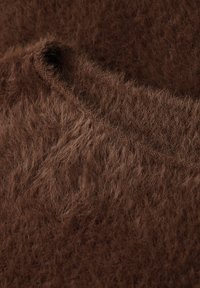 Brązowa, futrzasta tkanina o miękkiej, teksturowanej powierzchni. Charakteryzuje się stonowanym, bogatym kolorem oraz widocznym ściegiem wzdłuż krawędzi.