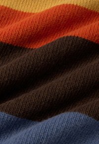 Gebreide stof met gedurfde strepen in geel, oranje, bruin en blauw. De textuur lijkt zacht met een gezellige, geribbelde afwerking.