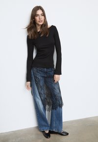 Črna majica z dolgimi rokavi, kombinirana z širokimi kavbojkami, ki imajo prosojno črno čipkasto prevleko. Gladke teksture, oprijete zgoraj, ohlapne spodaj.