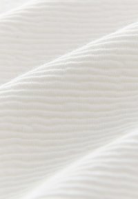 Tissu blanc avec un motif texturé et nervuré, présentant des plis doux et ondulés. La surface semble lisse et légère.