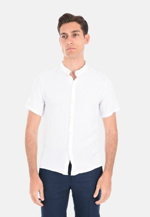 Camicia bianca di lino a maniche corte con colletto a band e bottoni frontali, caratterizzata da un tessuto leggermente strutturato e dettagli con risvolti sulle maniche.