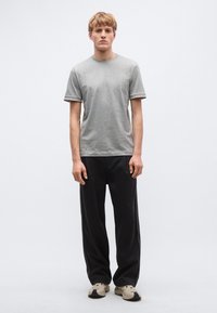 Szürke pamut rövid ujjú póló kerek nyakkivágással, fekete-fehér csíkos betétekkel az ujjakon, laza fekete nadrággal és sportcipővel párosítva.