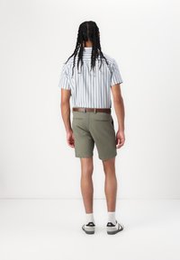 Chemise à manches courtes rayée bleu et blanc associée à un short vert olive et à une ceinture marron. Portée avec des chaussettes blanches et des sandales noires.