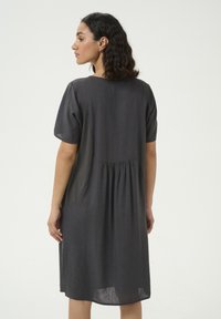 Robe grise à manches courtes, coupe loose, détail plissé au dos, poches latérales et longueur aux genoux, fabriquée en tissu léger.