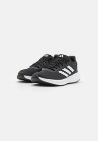 Scarpe sportive nere con tomaia testurizzata, design a tre strisce bianche e suola imbottita con un pronunciato motivo di battistrada.