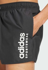 Crne sportske kratke hlače s elastičnim pojasom, sa bočnom džepom i istaknutim bijelim tekstom "adidas SPORTSWEAR". Lagan materijal.