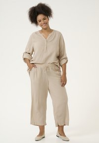 Top de lino beige con cuello tipo notch y mangas enrolladas, combinado con pantalones sueltos a juego que presentan una cinturilla elástica y cordón.