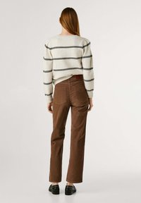 Trui met een crèmekleurige basis en zwarte strepen, gecombineerd met een bruine corduroy broek. De broek heeft een rechte snit en twee achterzakken.