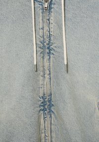 Jachetă din denim bleu deschis, cu fermoar și șnururi albe, având o textură netedă și un design minimalist; detalii de cusătură vizibile.