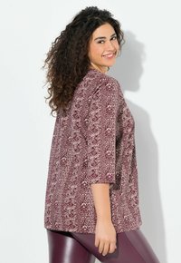 Burgunderfarbendes Top mit Muster und Dreiviertelärmeln, aus leichtem Stoff mit lockerer Passform, kombiniert mit lila engen Leggings.