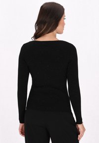 Der schwarze gerippte Langarmpullover verfügt über einen Scoop-Rücken, subtile Glitzerpartikel, eine taillierte Form und eine weiche Textur und wird mit lockeren schwarzen Hosen kombiniert.