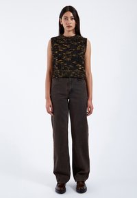 Svart och gult mönstrad ärmlös topp i kombination med högmidjade mörka denim-jeans, som har en avslappnad passform och raka ben.