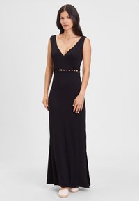 Black maxi dress with a deep V-neck, fitted bodice, and woven cut-out detailing at the waist. Smooth fabric, floor-length, side slit.