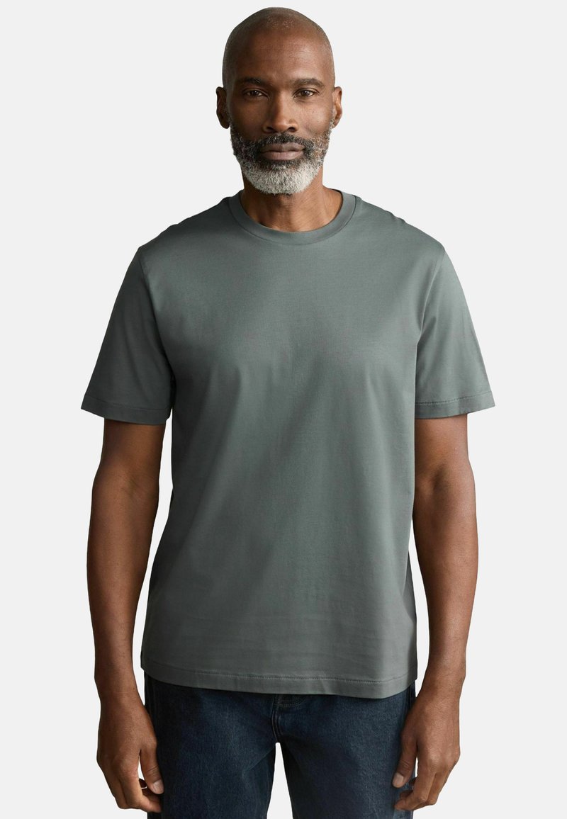 Kortærmet T-shirt i afdæmpet grøn, lavet af glat bomuld. Har en klassisk rund hals og lige bund, båret med mørke jeans.