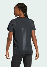 Donna con capelli intrecciati che indossa una maglietta sportiva nera a maniche corte con tre strisce verticali sulla schiena e leggings neri.