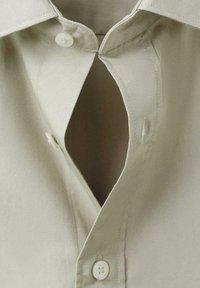 Camisa de color verde claro con botones, cuello puntiagudo y una apertura distintiva en forma de V en el cuello con botones a juego. Textura suave.