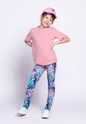 Ubrania dziecięce składające się z różowej koszulki z krótkim rękawem, kolorowych legginsów w marmurkowy wzór w odcieniach niebieskiego, różowego i białego, w połączeniu z białymi trampkami i różową czapką.
