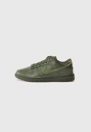 Niskie zielone sneakersy w kolorze oliwkowym z fakturą przypominającą łuski gada, sznurówkami i logo Nike Swoosh po boku na jednolitym tle.