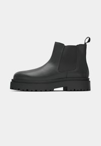 Bottines Chelsea en cuir noir avec des panneaux élastiques sur les côtés, semelle en caoutchouc épaisse et tirette à l'arrière, présentant une finition lisse et un profil de semelle robuste.