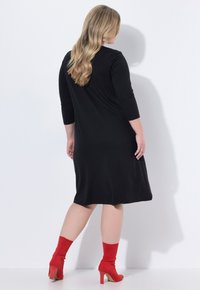Robe noire à manches trois-quarts, de longueur genou, au texture douce. Portée avec des bottines rouges et des chaussettes assorties.