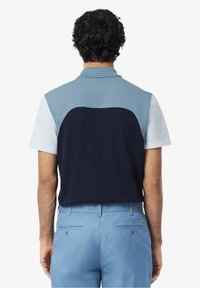 Short-sleeved polo with a color-block design in light blue, navy, and pale blue, featuring a classic collar and textured fabric finish.