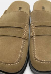 Pantofi slip-on din suede maro cu un design mocasin, având cusături decorative și o sole din cauciuc negru.