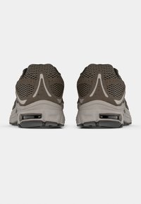 Καφέ πλέγμα αθλητικά παπούτσια με υφασμένα σουέτ στοιχεία, διπλή στρώση στη μεσαία σόλα και μοναδικό σχεδιασμό της φτέρνας ορατό από την πίσω όψη.