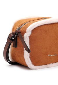 Borsa a mano in suede beige con bordo in pelliccia sintetica bianca, forma rettangolare, chiusura con zip e tracolla e dettagli in pelle marrone. Dettaglio del logo in oro visibile.
