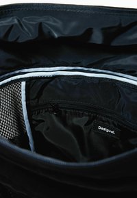 Black bag interior, featuring smooth fabric, zippered compartments, and mesh pocket. Notable brand label: Desigual.