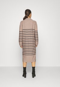 Dlouhé pletené šaty světle béžové barvy s tmavými vodorovnými pruhy. Mají límec a dlouhé rukávy, rovný střih sahající do poloviny lýtek.