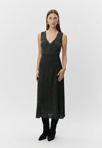 Zwart, mouwloos maxi-jurk met V-hals en geplooid ontwerp. Gemaakt van geribbelde, gestructureerde stof. Gepaarde met knielange zwarte laarzen.