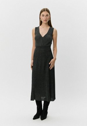 Zwart, mouwloos maxi-jurk met V-hals en geplooid ontwerp. Gemaakt van geribbelde, gestructureerde stof. Gepaarde met knielange zwarte laarzen.