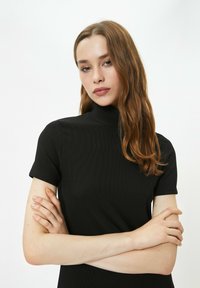 Schwarzer gerippter Rollkragenpullover mit kurzen Ärmeln und einer eng anliegenden Passform. Der Stoff wirkt glatt und leicht dehnbar.