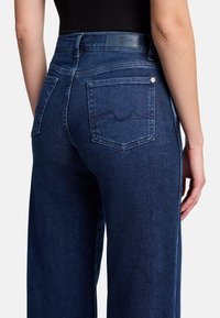 Ciemnoniebieskie spodnie z wysokim stanem o gładkiej, lekko elastycznej strukturze. Posiadają dwie tylne kieszenie z delikatnym przeszyciem oraz skórzaną metkę na pasku.