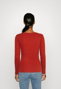 Rostfärgad långärmad topp i mjukt trikåtyg, med en lätt rundad halsringning och figurnära passform. Buren med ljusblå jeans.