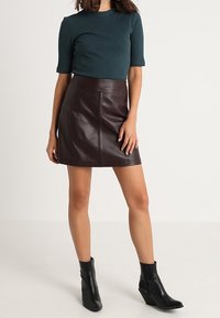 Türkisfarbener, gerippter Stricktop mit kurzen Ärmeln, kombiniert mit einem bordeauxroten Leder-Minirock, abgerundet mit schwarzen, hohen Stiefeletten.