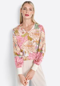 Floral-print blouse with a V-neck, featuring pink and beige flowers, long sleeves, and ribbed cuffs in white. Smooth fabric with a light texture.