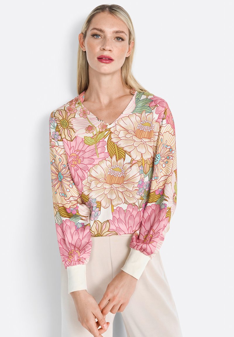Floral-print blouse with a V-neck, featuring pink and beige flowers, long sleeves, and ribbed cuffs in white. Smooth fabric with a light texture.