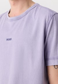Fialové bavlněné tričko s kulatým výstřihem, na levé straně hrudi zdobené malým vyšitým logem "BOSS" ve stejném odstínu. Hladká textura.