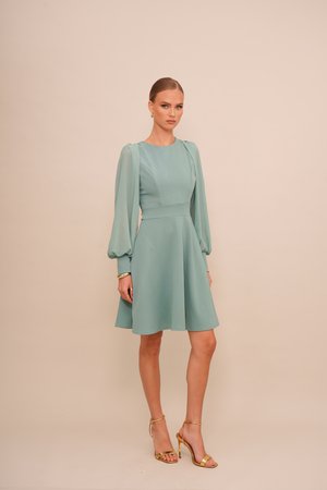 Un vestito verde menta con un corpetto aderente e una gonna svasata. Presenta maniche lunghe e trasparenti a palloncino ed è completato da tacchi a strappo dorati.
