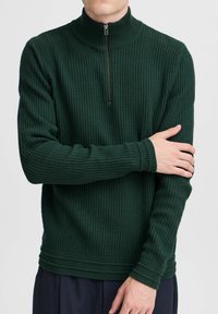 Dunkelgrüner, strukturierter Strickpullover mit hohem Kragen und halbem Reißverschluss. Verfügt über eng anliegende Bündchen und einen gerippten Saum, der eine klare Silhouette schafft.