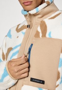 Giacca in pile con un motivo astratto beige, blu e marrone; presenta un colletto alto, una tasca con zip e una texture morbida.