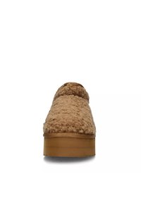 Zapato slip-on color beige con parte superior difusa y texturada, y suela gruesa de color marrón claro, que presenta una puntera redonda y un diseño minimalista.