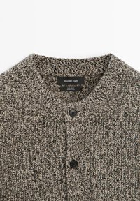 Wollstrickjacke mit Rundhalsausschnitt, bestehend aus einem strukturierten grauen und beigen Strickmuster. Verfügt über schwarze Knöpfe und ein Markenlabel innen.