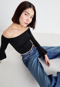 Black off-the-shoulder long-sleeve top paired with light blue wide-leg jeans. Smooth fabric, fitted at the waist, flared sleeves.