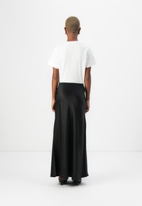 Weißes kurzärmeliges Oberteil und schwarzer Satin-Maxirock, der eine glatte Textur, eine taillierte Passform und eine fließende Silhouette aufweist. Schwarze Absätze runden den Look ab.