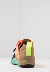 Rückansicht eines mehrfarbigen Nike Free Sneakers mit tanfarbenem, orangefarbenem, neongelben Pull-Tab und türkisfarbenen Sohlenakzenten vor einem weißen Hintergrund.