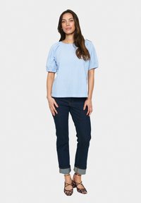 Blusa a righe blu chiaro con maniche a sbuffo, abbinata a jeans scuri, che mette in mostra un fit rilassato. Le calzature presentano un design a stampa leopardata.