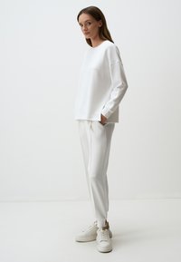 Witte sweatshirt met lange mouwen, losse pasvorm, zijsplitten, gecombineerd met witte tapered sweatpants en witte sneakers. Glad stoftextuur.